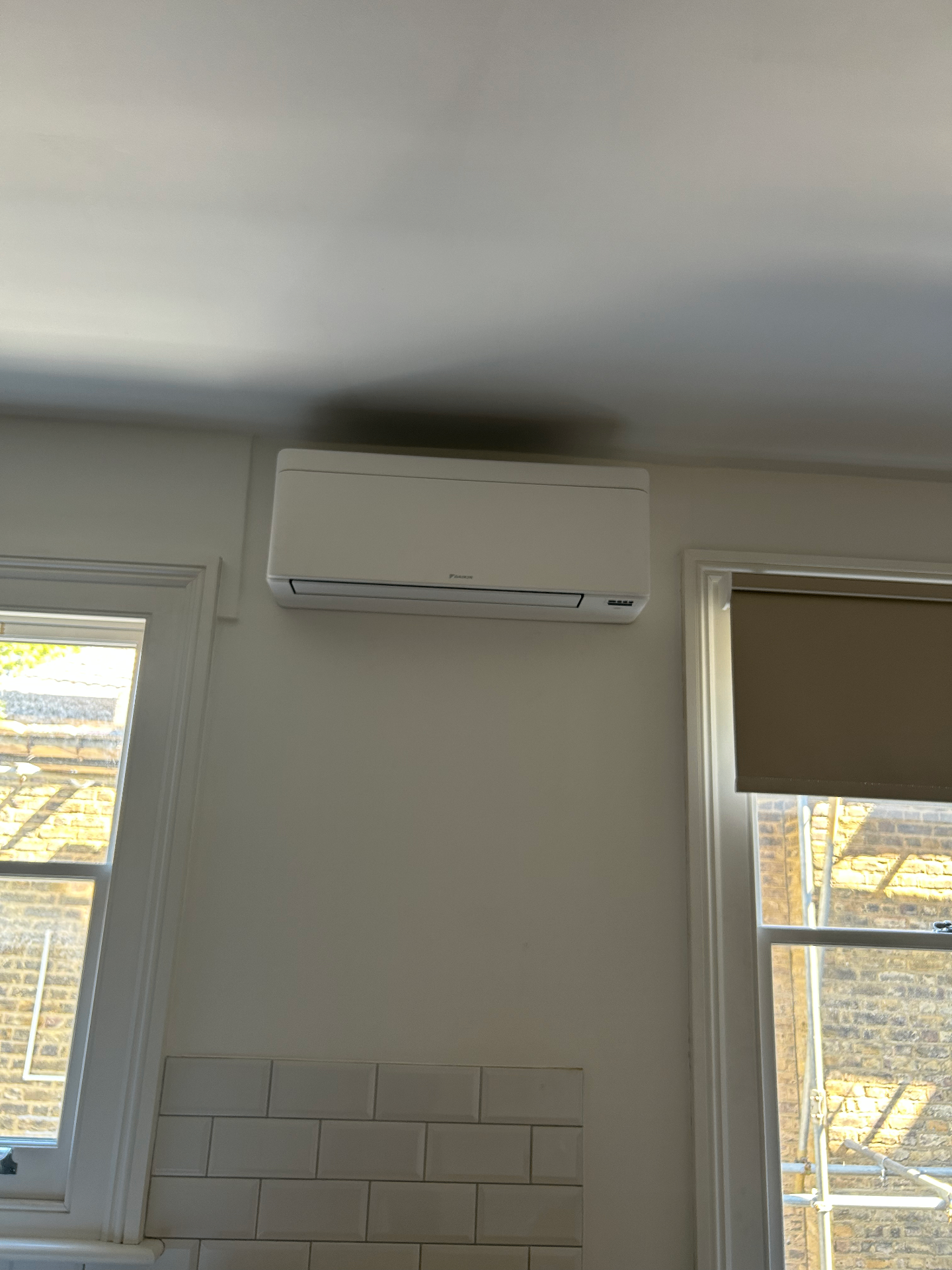 White wall-mounted air conditioning unit installed high between two windows in a Fulham property