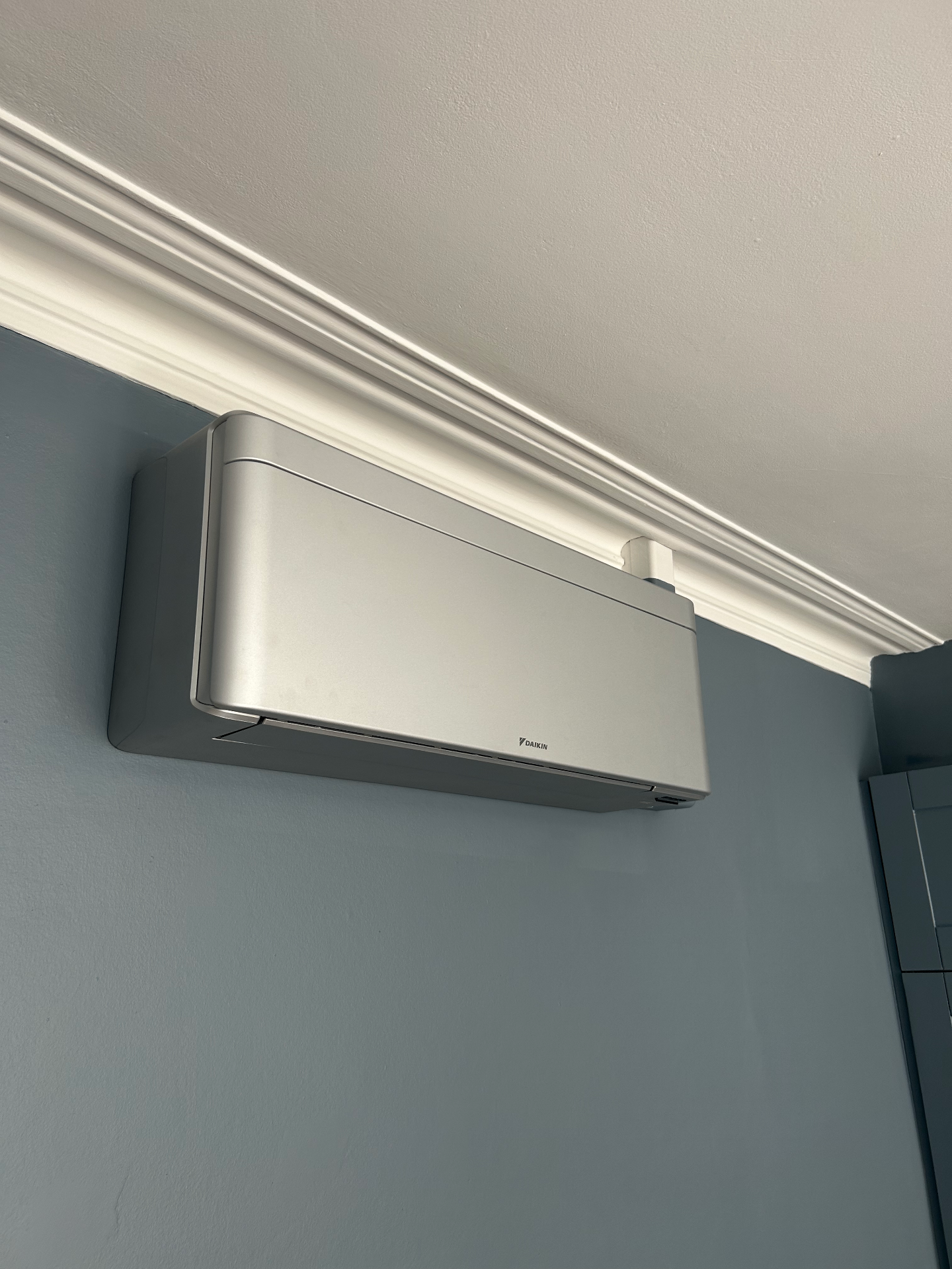 Silver wall-mounted air conditioning unit installed neatly below decorative ceiling cornicing in Fulham