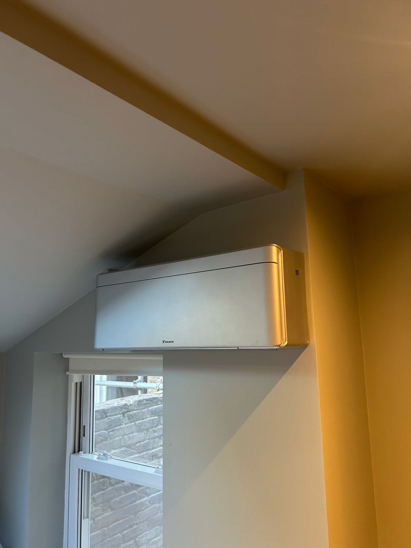 Silver air conditioning unit fitted on a sloped wall above a window in Fulham